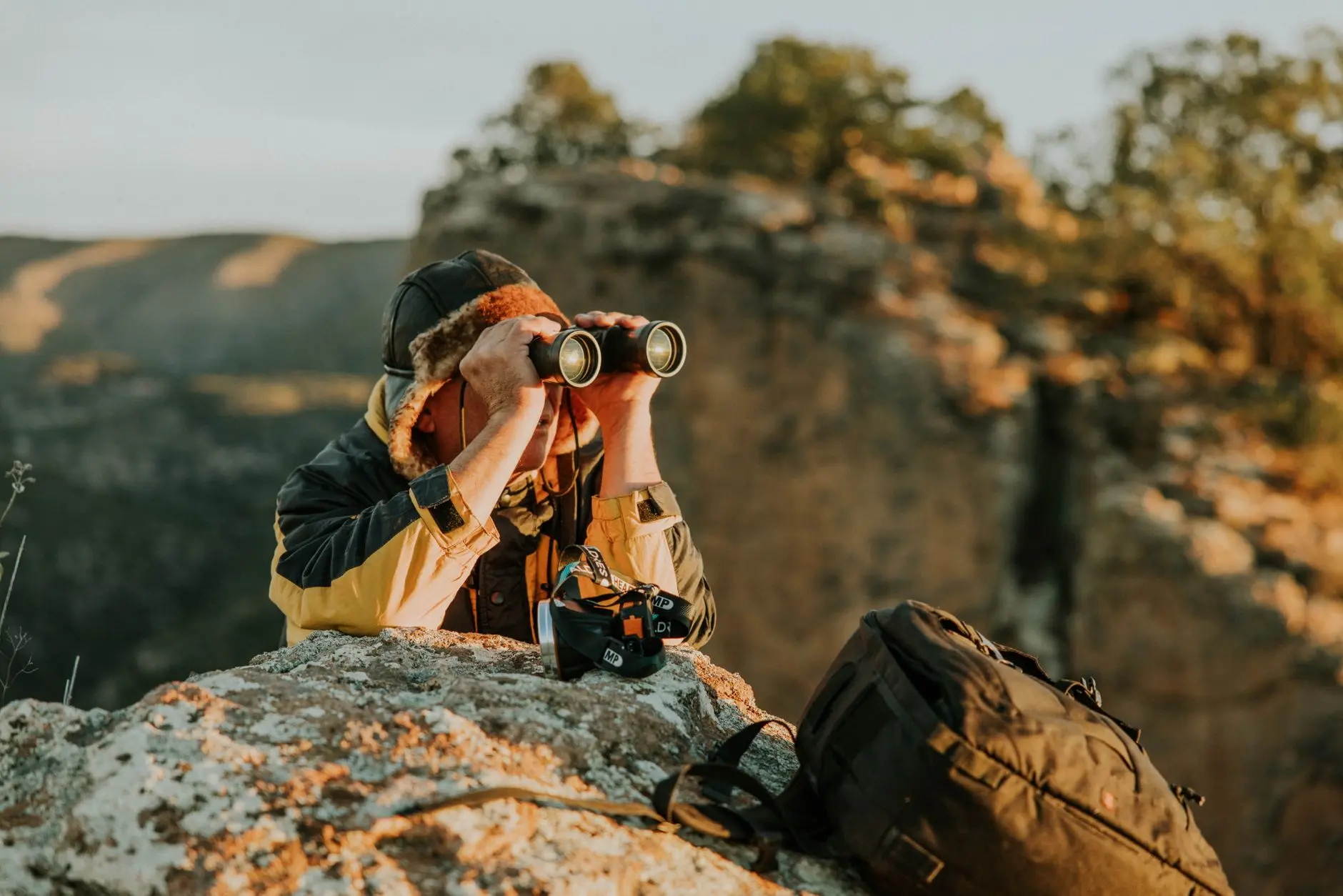 A pair of binoculars placed outdoors, lit by natural light, with greenery in the background.